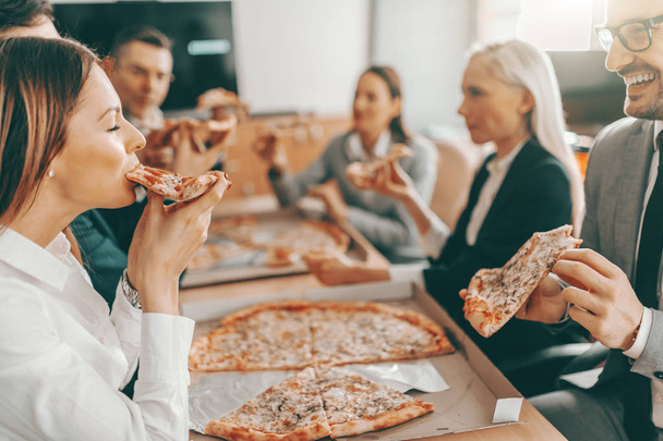 Eine kleine Gruppe fröhlicher Kollegen in festlicher Kleidung isst gemeinsam Pizza zum Mittagessen. Es ist schwer, eine Mannschaft zu schlagen, die zusammenhält. - Foto, Bild