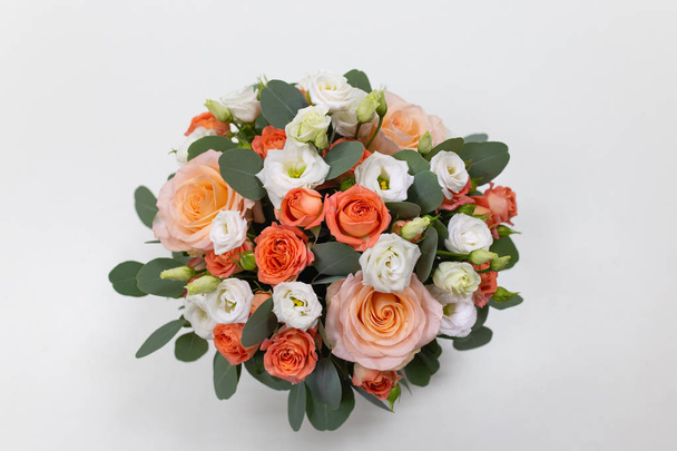 Delicate floral arrangement of roses (white, pink, orange) and green eucalyptus leaves in a round white cardboard box on a light background - 写真・画像