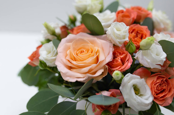 Delicate floral arrangement of roses (white, pink, orange) and green eucalyptus leaves in a round white cardboard box on a light background - Zdjęcie, obraz