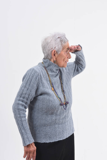 Senior vrouw met hand op de voorgrond op zoek weg op witte achtergrond - Foto, afbeelding