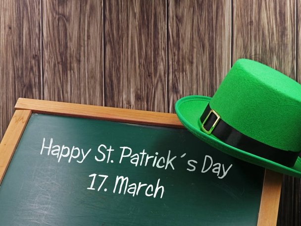 Happy St. Patricks Day chalk text with green hat on blackboard and wooden background for copy space - Photo, image