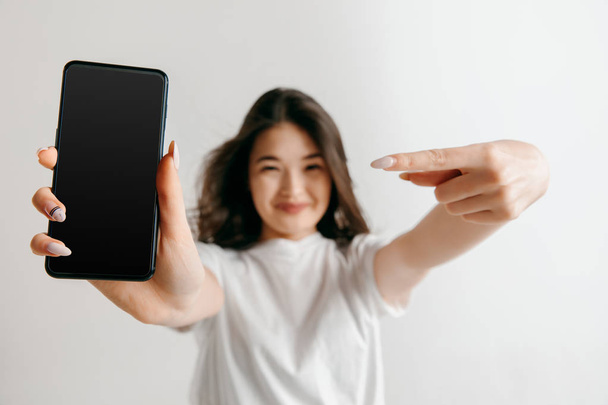 Portrait of a confident casual asian girl showing blank screen of mobile phone - Фото, изображение
