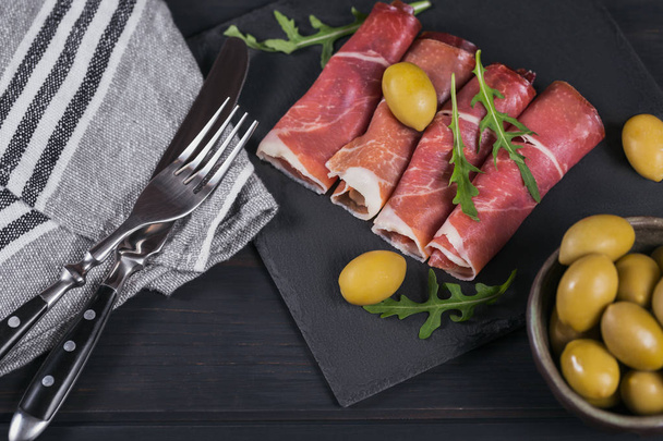 Black stone platter with slices of cured ham or Spanish jamon se - Foto, afbeelding
