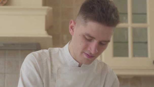 Close up portrait of young concentrated cook in chef uniform preparing food at home in the kitchen. Concept of food preparation - Imágenes, Vídeo