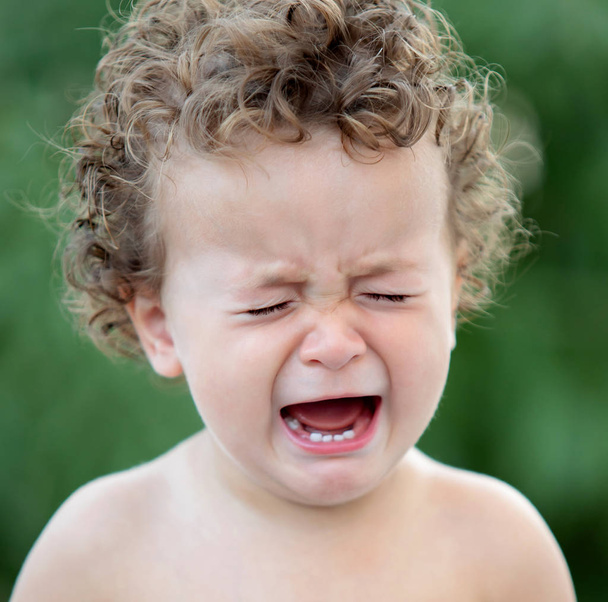 trauriges Baby mit lockigem Haar weint im Garten - Foto, Bild