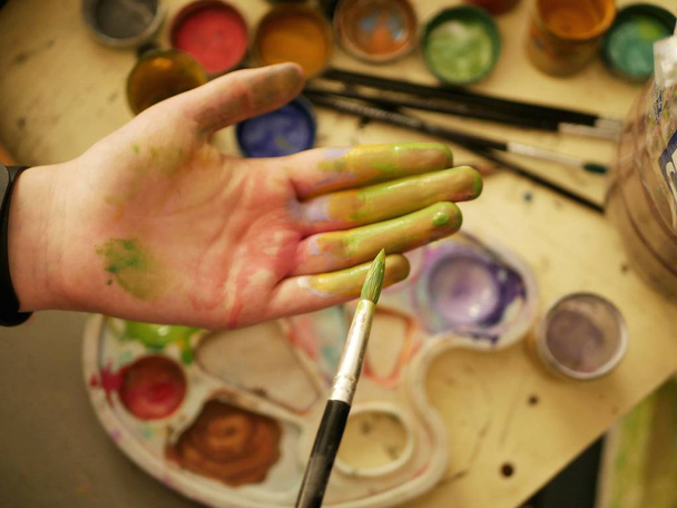 Рука в фарбі студента художньої школи на тлі палітри і фарб, процес навчання і виховання
 - Фото, зображення