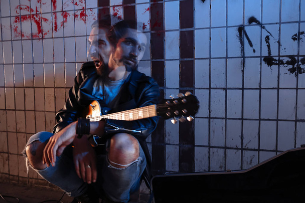 Een straatmuzikant speelt op gitaar in de onderdoorgang. Twee gezichtsuitdrukkingen uiten verveling en woede. - Foto, afbeelding