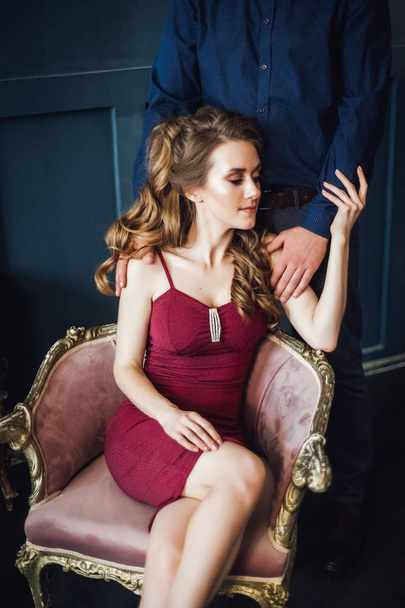 Beautiful woman sitting in vintage armchair with man standing behind indoor - Фото, изображение