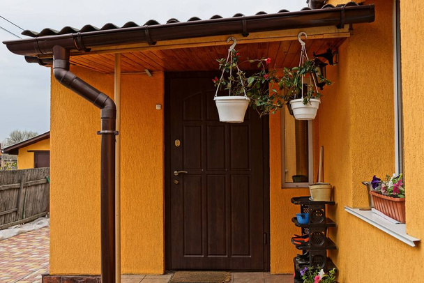 Veranda eines braunen Privathauses mit geschlossener Tür und Blumentöpfen - Foto, Bild