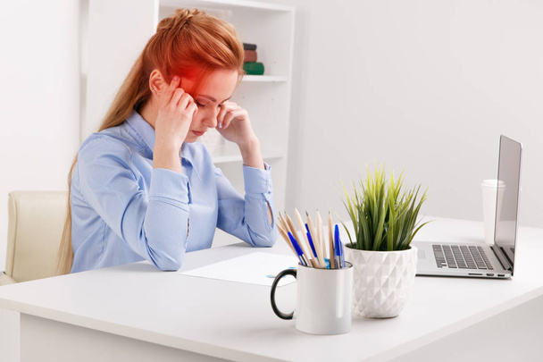 Молодая офисная девушка сидит на своем рабочем месте и чувствует себя плохо. У женщины болит голова.
. - Фото, изображение