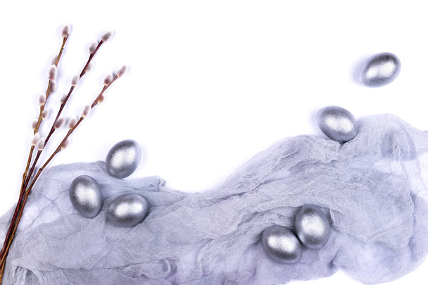 Серебряные пасхальные яйца с ветками ивовых кошек на серой марли ткани изолированы на белом фоне
.  - Фото, изображение