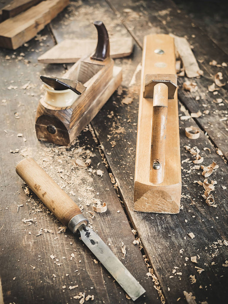 Старый деревообрабатывающий ручной инструмент: деревянный самолет, долото и в столярной мастерской на грязном деревенском столе с видом на задний план из опилок
 - Фото, изображение