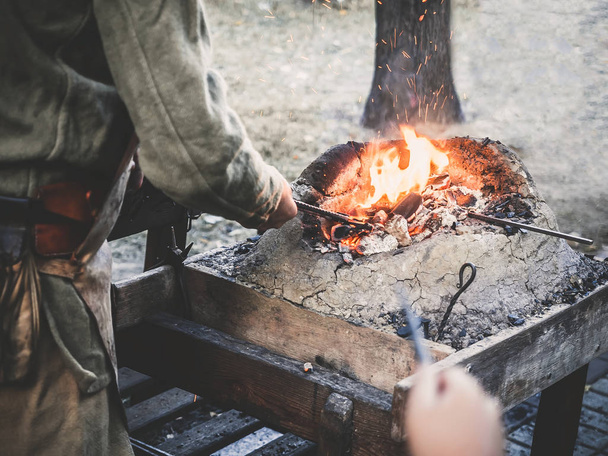 Le forgeron tient la billette sur des charbons chauds dans un four à argile. forgeron chauffage fer fer épée fabrication marche forge
 - Photo, image