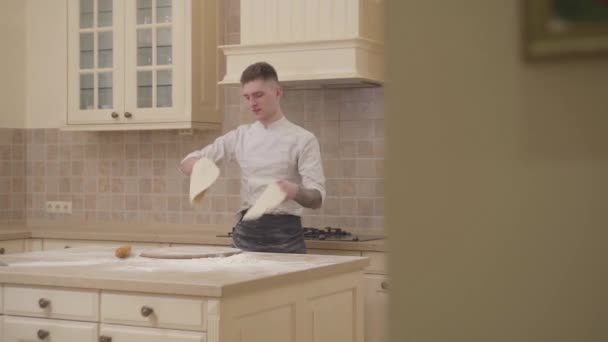 Nuori kaveri pyörii ja heittää kaksi levyä pizzataikinaa keittiössä kotona. Ammattimainen pizzaiolo tekee pizzaa. Ruoanvalmistuksen käsite. Hidastus
. - Materiaali, video