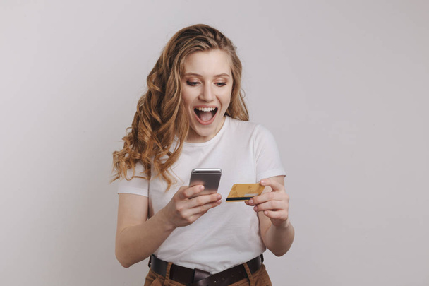 Feliz chica bonita haciendo compras en línea por su teléfono y tarjeta de crédito naranja
. - Foto, imagen