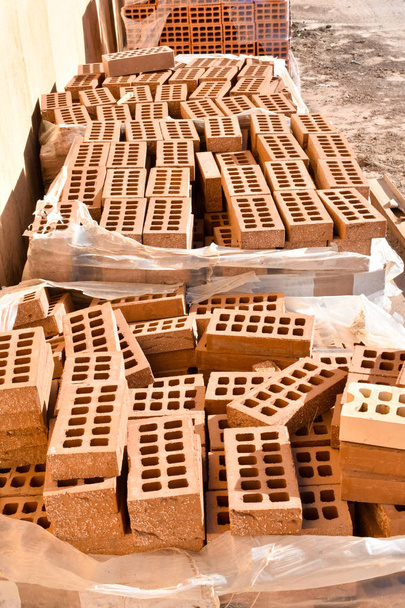 a wooden pallet plenty of old stacked red bricks in rows. Behind there is other pile of red bricks wrapped with plastic. - Photo, Image