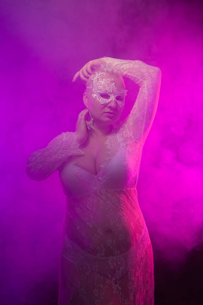 charming plump girl with short hair in white lace lingerie. plus size woman stands in a bra, panties and a transparent dress with mask. - Φωτογραφία, εικόνα