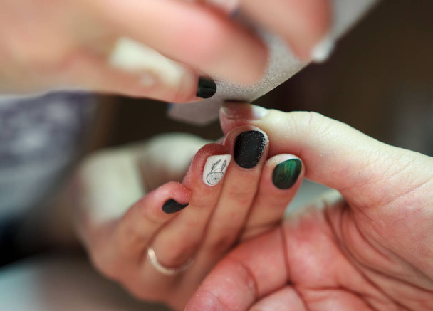 nagelservice manicure zaagt en gladstrijkt de nagels van de klant met behulp van een bestand. reportage schieten - Foto, afbeelding