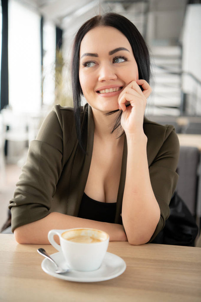 Restoranda oturan güzel siyah saçlı kadın. Uzağa bakıyor ve gülümsüyor, kahve içme - Fotoğraf, Görsel
