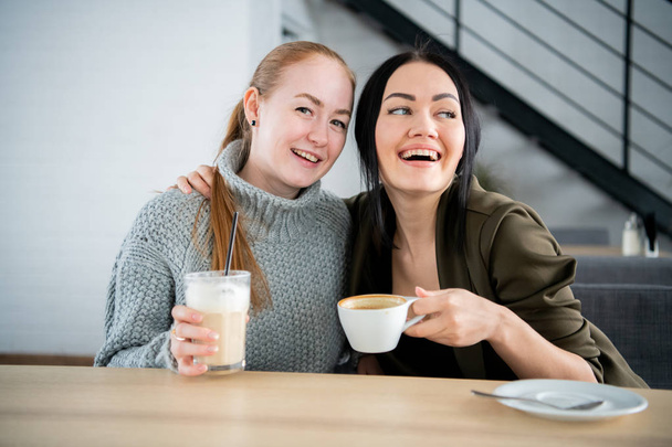 Zwei Frauen halten Kaffeebecher in der Hand. Morgens auf der Couch sitzen und über den Job reden. eine Tasse Kaffee macht Körper und Gehirn frisch. - Foto, Bild