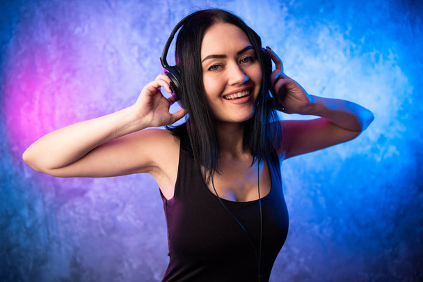Colorido retrato en ligth azul y rosa de una joven DJ con auriculares y disfrutando de una música electrónica. - Foto, imagen