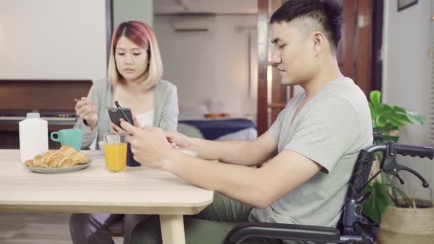 Bir tekerlekli sandalyede Mutlu tatlı Asya çift adam kahvaltı, süt, ekmek tahıl ve sabah uyandıktan sonra haber okuma cep telefonu kullanarak. Karı ve eşi birlikte yemek yiyor.. - Video, Çekim