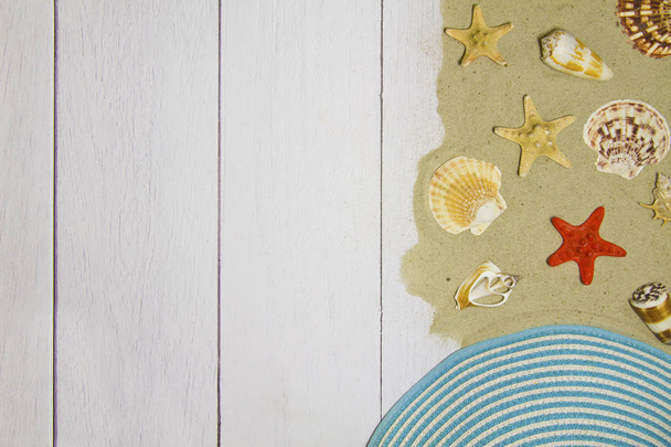 Sea shells, stars, hat on a light wooden background with sand, top view - Foto, afbeelding