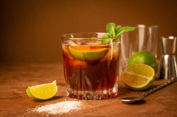 Cocktail van rum en Cola ijsblokjes en limoen in een glazen Goblet op een donker bruine achtergrond. Sterke alcoholische drank. - Foto, afbeelding