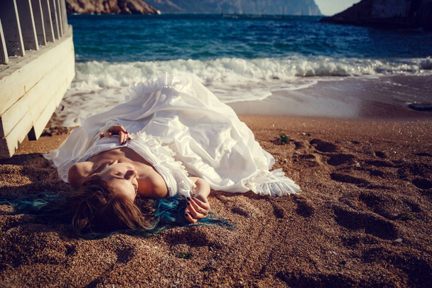 Hermosa chica con el pelo azul y en un vestido vintage blanco mira al mar. En sus manos un hermoso espejo antiguo, en el que el mar se refleja. Portada del libro
 - Foto, imagen