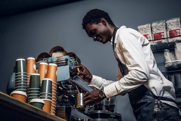 Barista n λευκό πουκάμισο και ποδιά κάνει καφέ στη μηχανή του καφέ σε μια καφετέρια - Φωτογραφία, εικόνα