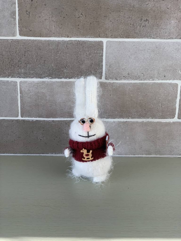 Рука зроблена милою розумною в'язаною іграшкою кролика або зайцем в червоному светрі з конем і книгою на цегляному стіні, що стоїть на столі
 - Фото, зображення