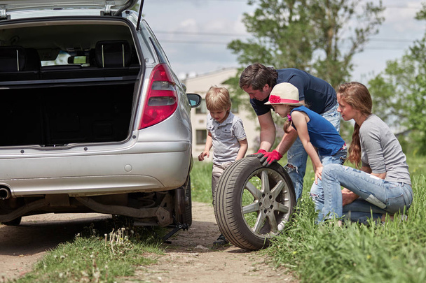 children help their father to replace the car tire. - Photo, Image