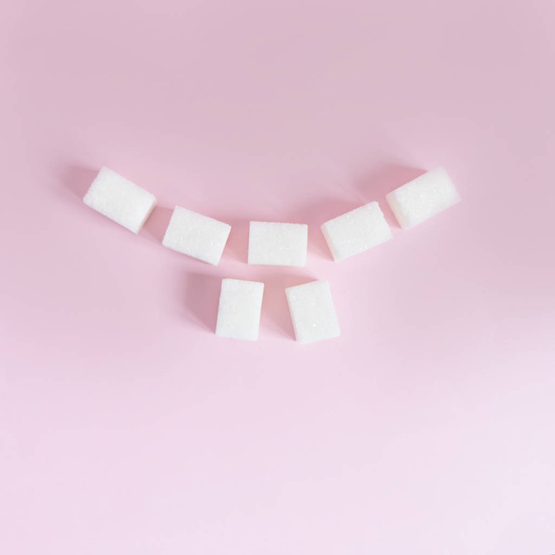 cubes of white sugar are laid out in the form of a smile with teeth on a pink background - Foto, afbeelding