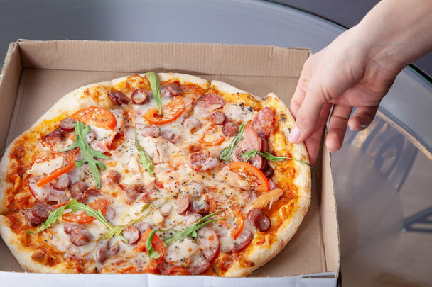 Vrouwelijke hand neemt een lekkere plak van pizza uit het vak. - Foto, afbeelding