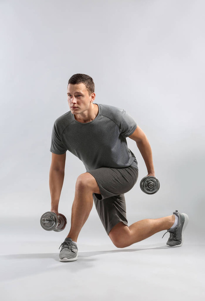 Sporty young man training with dumbbells against grey background - Foto, afbeelding