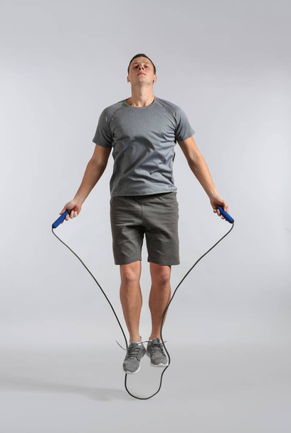 Sporty young man jumping rope against grey background - Фото, изображение