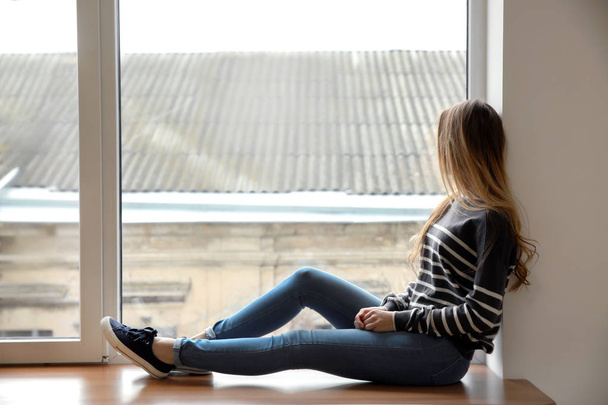 Beautiful young woman sitting on window sill - Photo, image