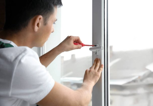 Молодой рабочий ремонтирует окна в квартире
 - Фото, изображение