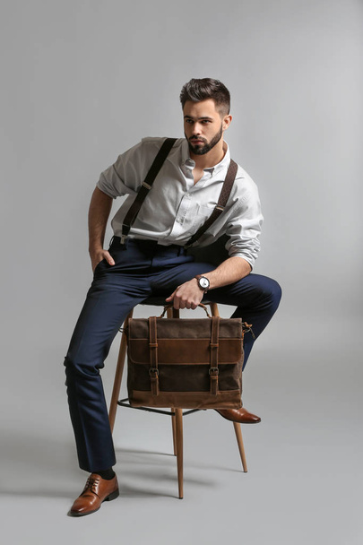 Fashionable young man with bag sitting on chair against light background - Fotoğraf, Görsel