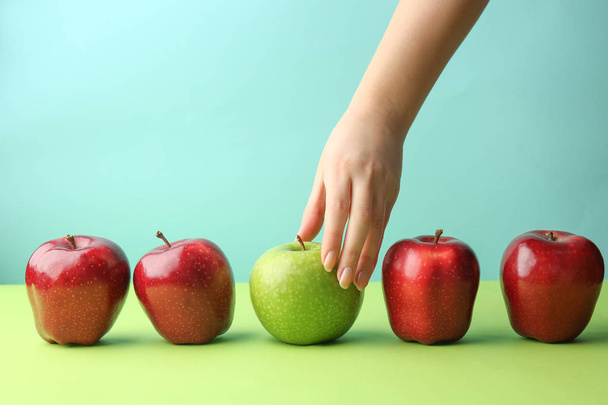 Vrouwelijke hand met lekkere appels op kleur achtergrond. Concept van uniciteit - Foto, afbeelding