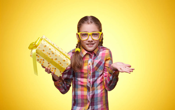 Emotionele tiener meisje met een gift op een gele achtergrond - Foto, afbeelding