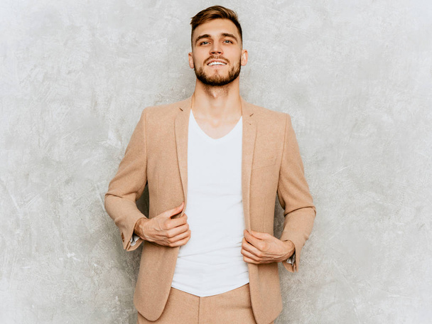 Portrait of handsome serious modern hipster lumbersexual businessman model wearing casual beige suit. Fashion stylish man posing against gray wall - Фото, зображення