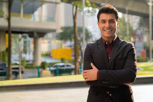 Jeune homme d'affaires hispanique heureux souriant avec les bras croisés à l'extérieur
 - Photo, image