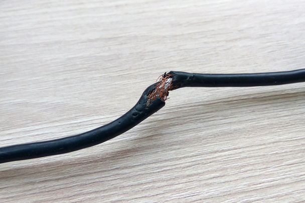 Cable eléctrico negro dañado sobre fondo de madera. Cable eléctrico peligroso de alimentación rota
 - Foto, Imagen