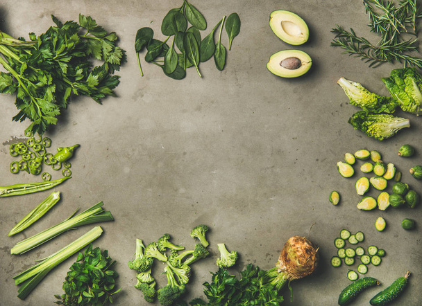 Healthy vegan ingredients layout. Flat-lay of whole and cut green vegetables and herbs over concrete background, top view, copy space. Vegetarian, clean eating concept - Photo, image
