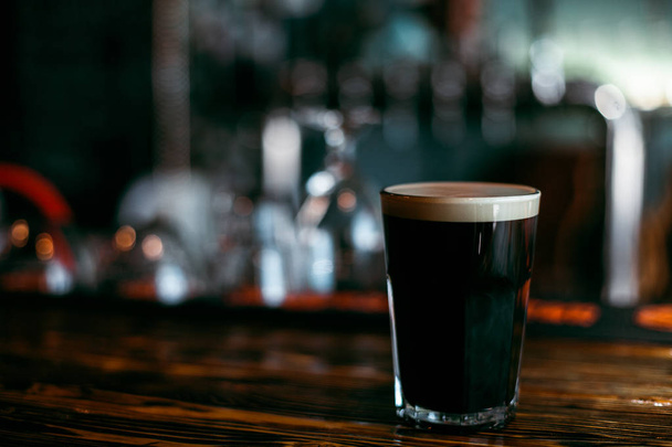 Dark beer. Stout. In a glass grocery. On a wooden table in the bar. - Foto, afbeelding