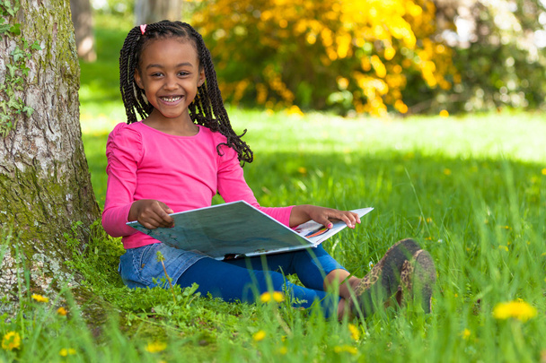 Outdoor portrait of a cute young black little girl reading a boo - Фото, изображение