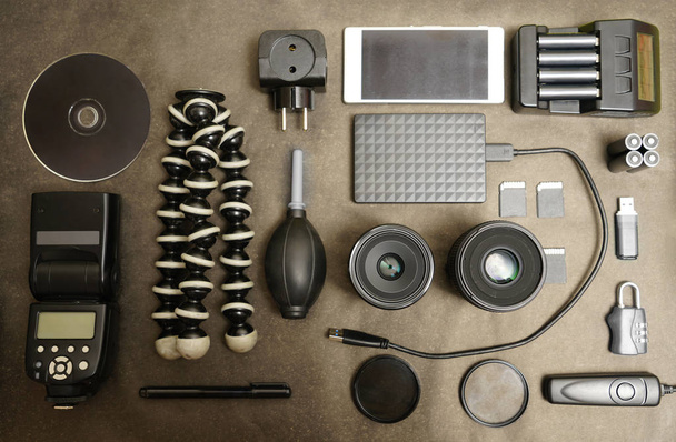 Workspace of photographer. Top view with black table, photo flas, lens, smartphone, remote control, compact disk and battery charger.  - Foto, Imagen
