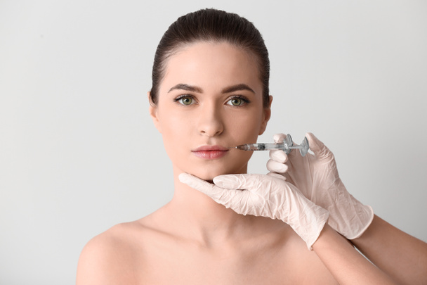 Jovem mulher a receber injeção no rosto sobre fundo claro
 - Foto, Imagem