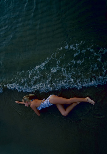 zobrazení shora. Krásná mladá žena se světlými kudrnatými dlouhými vlasy a bílým plavým oblečenými na mokrém písku na mořské pláži. letní den. Létě - Fotografie, Obrázek